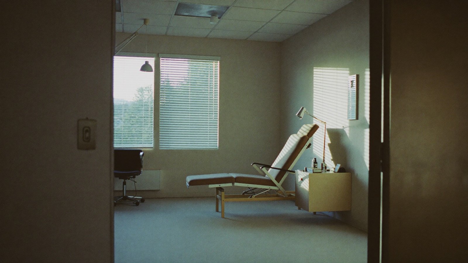 Quiet clinic consultation room with morning light through venetian blinds