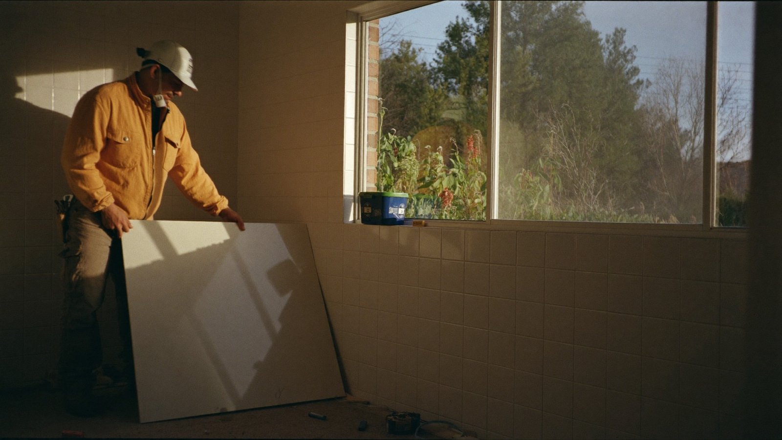 Contractor setting a large tile panel in a home renovation, lit by late afternoon sun